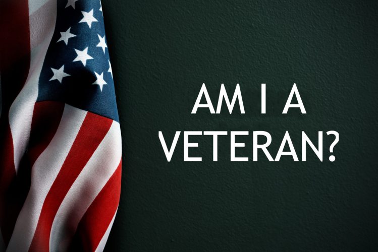 An American flag hanging to the side of a green chalk board wall that reads, "AM I A VETERAN?"