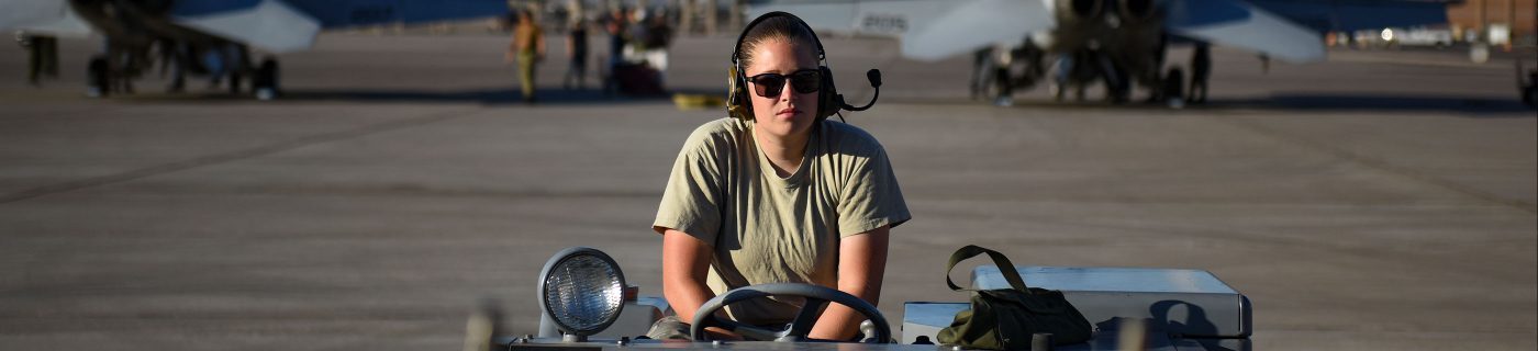 Military person in jeep with planes in background