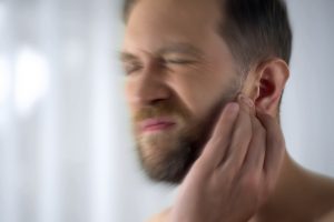 Man winces and rubs his ear due to tinnitus (ringing in the ears)
