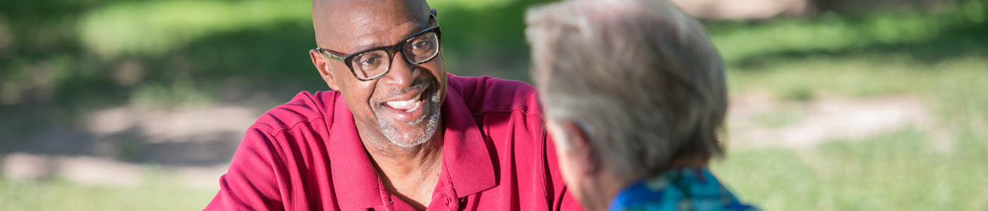 Man with glasses talking to another man outdoors
