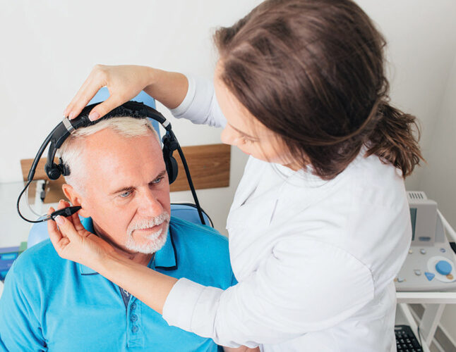 Female doctor examining elderly patient ear , using special medical equipment, at doctors office